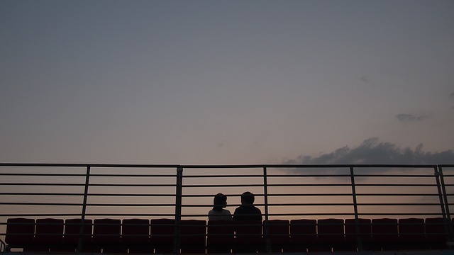 Dvaja ľudia sedia za zábradlím pri západe slnka.jpg